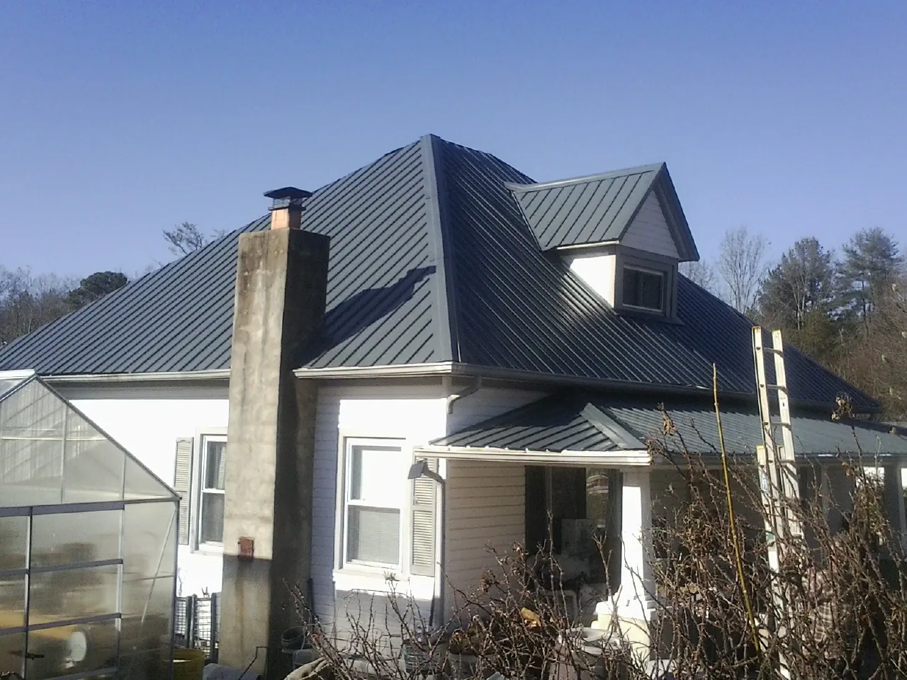 Dark blue standing seam metal roof on a white farmhouse with dormer — Slate & Tile Roof Repair by Roofing Brothers in Lenox