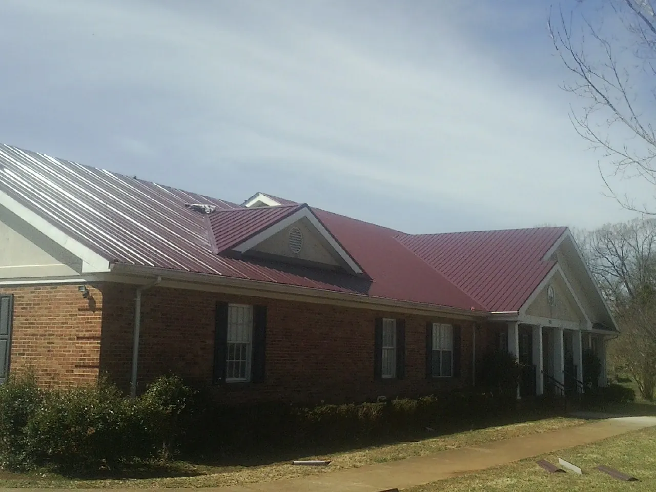 Red metal roof with gabled entries on a long brick building, from a Hail Damage Roof Repair job in Lenox