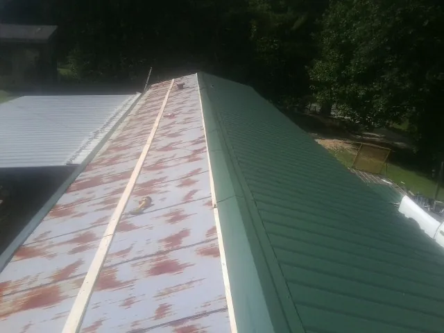 Old rusted panels beside newly installed green metal roofing — Wind Damage Roof Repair by Roofing Brothers in Lenox