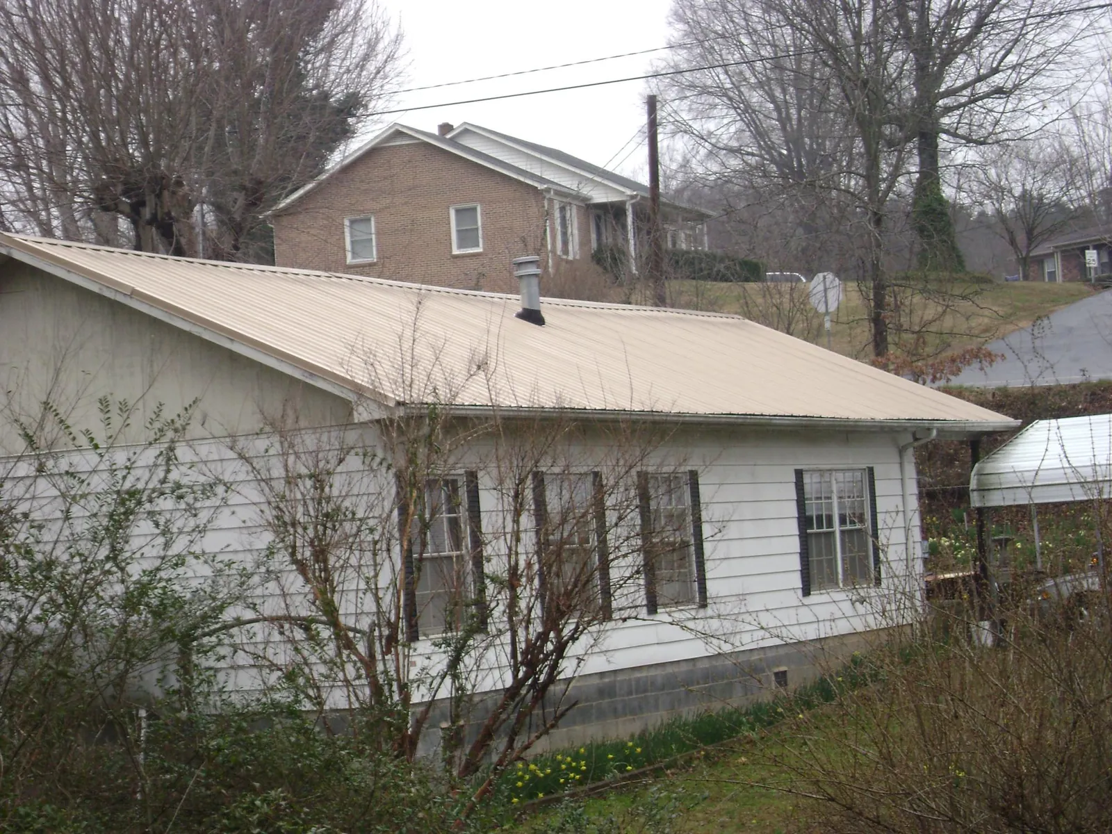 Tan metal roof on a white sided house set into a hillside — Commercial Roofing by Roofing Brothers in Lenox